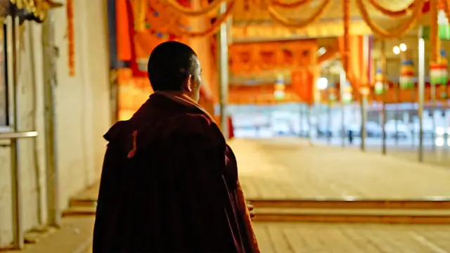 Um monge tibetano de costas durante as orações matinais no mosteiro de Kirti