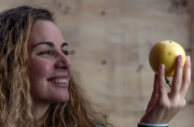 Una mujer sonriente mira un maracuyá que sostiene en la mano
