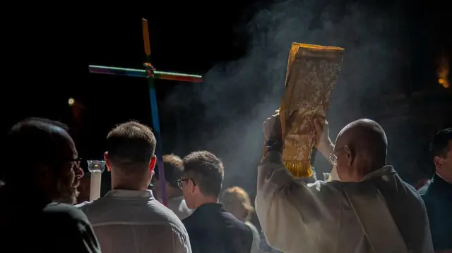 Mężczyzna trzymający krzyż przybywa z innymi członkami społeczności LGBTQ+ na mszę do kościoła Il Gesù w centrum Rzymu we Włoszech