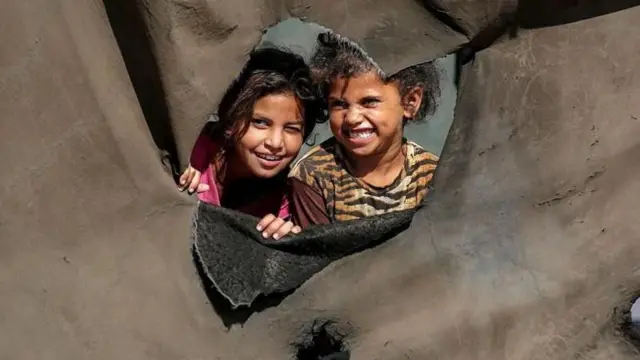 युद्धामुळे विस्थापित झालेल्या लोकांच्या छावणीतल्या तंबूच्या आडून डोकावत असलेली मुले (7 ऑक्टोबरचा फोटो).