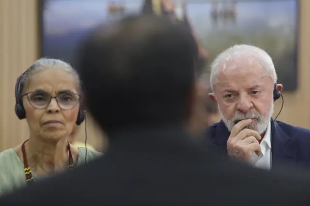Marina Silva e Lula compenetrados durante reunião na COP; eles usam fones de ouvido para tradução