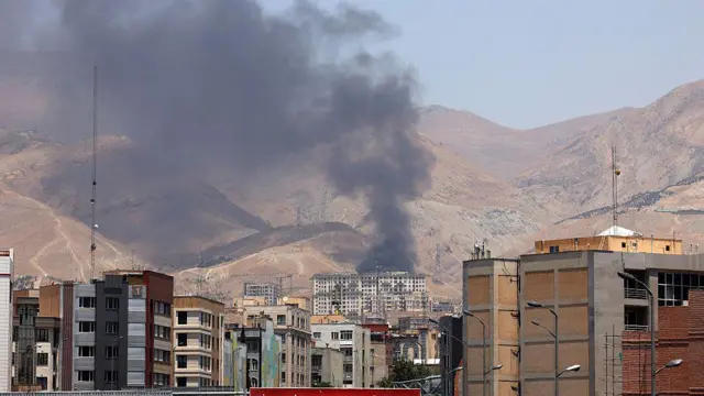 Tahran'ın kuzeybatısındaki Şahran petrol deposundan dumanlar yükseliyor, dağlık bir alana konumlu depo ile aynı manzarada binalar var.