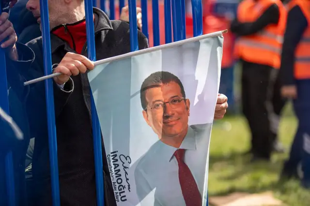 elinde imamoğlu bayrağı tutan bir adam bariyerlerin arkasında