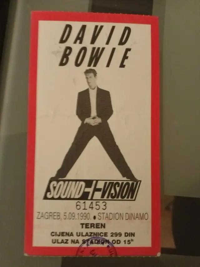 Koncertna ulaznica na kojoj je Dejvid Bouvi u crnim pantalonama i sakou, ispod kojeg ima belu košulju