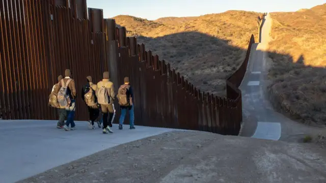 Immigrants from India walk next to the Trump-built U.S.-Mexico border fence after crossing into Arizona on January 19, 2025 near Sasabe, Arizona. They had passed through a gap in the fence after being delivered by smugglers to a remote area in the Sonora Desert. While immigrant crossings have been down sharply in the last year, the incoming Trump administration has vowed to "seal" the border completely.
