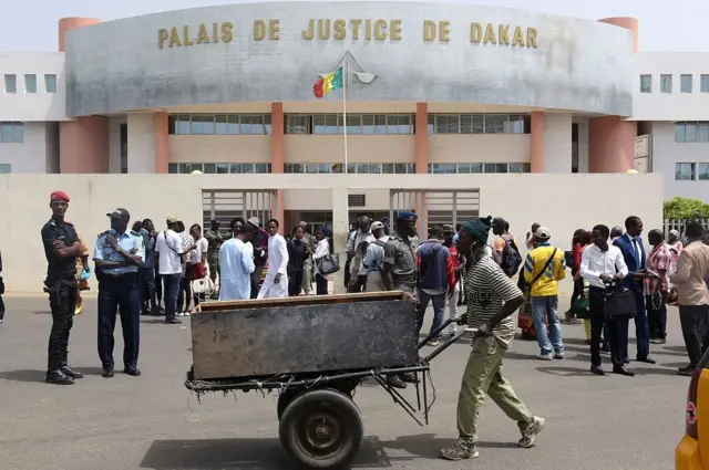 Un homme pousse une poussette devant des passants et des membres des forces de sécurité sénégalaises postés devant le tribunal de Dakar.