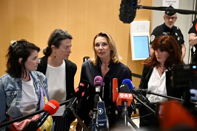 Amelie, etrafında üç kadınla birlikte mikrofonlara konuşurken