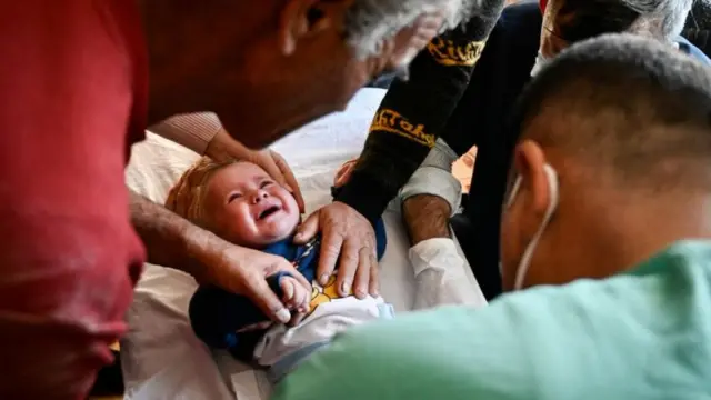 Bebê chorando rodeado por homens e médicos