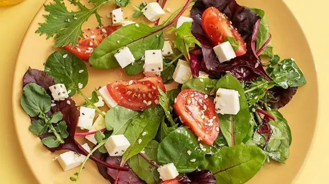 পনির দেওয়া সতেজ সবজির সালাদ হলুদ রঙের একটি প্লেটে। পাশে একটি বোতলে ড্রেসিংয়ের তেল