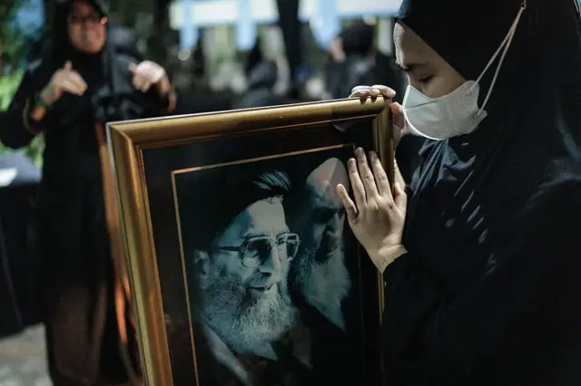 Seorang perempuan Muslim Indonesia memegang potret Pemimpin Tertinggi Iran Ali Khamenei (kiri), saat peringatan belasungkawa di Pusat Kebudayaan Islam Jakarta di Jakarta pada Minggu (01/03).