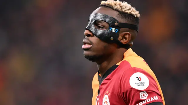 Victor Osimhen porte un chandail Galatasaray rouge et orange et un masque de protection noir avec « VO9 » sur le côté gauche.