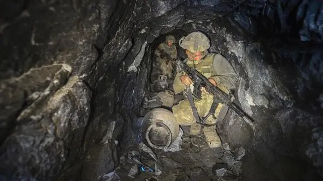 Kamuflajlı iki asker bir mağarada ilerliyor, ellerinde silahları var - 15 Ağustos 2017