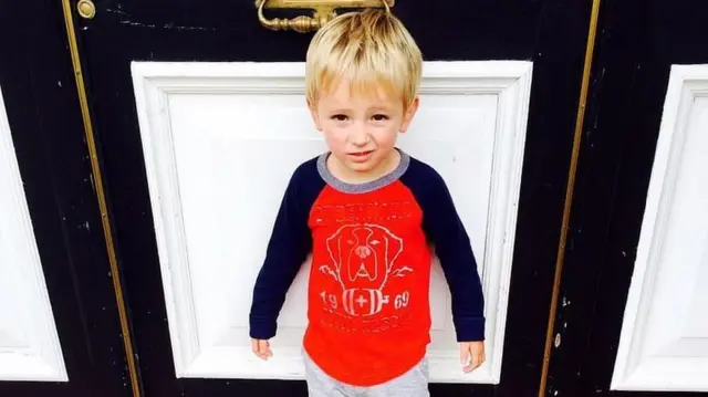 Tommy quando pequeno. É um menino loiro que usa uma blusa de mangas compridas com a estampa de um cachorro.