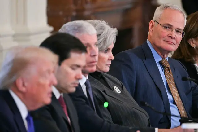 Donald Trump hablando y a lo lejos lo ve el presidente de ExxonMobil, Darren Wood