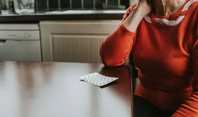 Mulher sentada em uma mesa com embalagem de remédios em sua frente