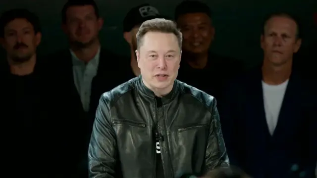 Elon yambaye ijaketi y'uruhu y'umukara, arimo kuvuga.