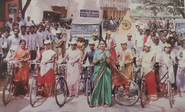 تصویر شیلا رانی چونکات با ساری سبز که در مقابل ده ها زن بایسکل سوار ایستاده است. 