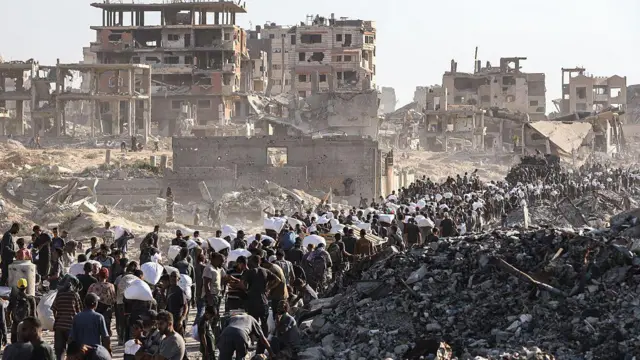 Multidões de palestinos se reúnem em um centro de distribuição de ajuda humanitária perto da passagem fronteiriça de Zikim, em Gaza, cercada por escombros e prédios bombardeados.