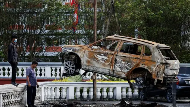 सिंहदरबार परिसरमा क्रेनको सहायताले उठाइँदै गरेको आगो लगाइएको एउटा कार। दुई जना व्यक्ति उक्त काम नजिकबाट नियालिरहेका छन्