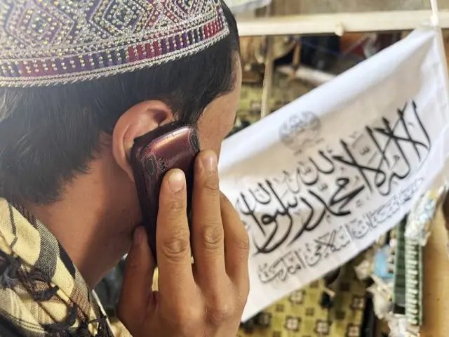 یک مرد در مقابل پرچم طالبان در حال صحبت با تلفون