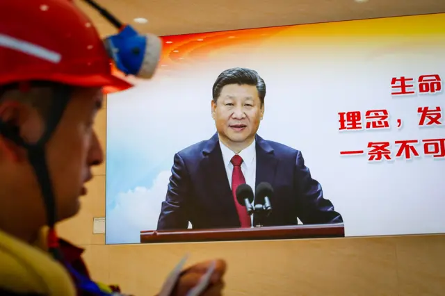 Un minero y en el fondo un televisor que muestra al presidente chino dando un discurso en 2023.