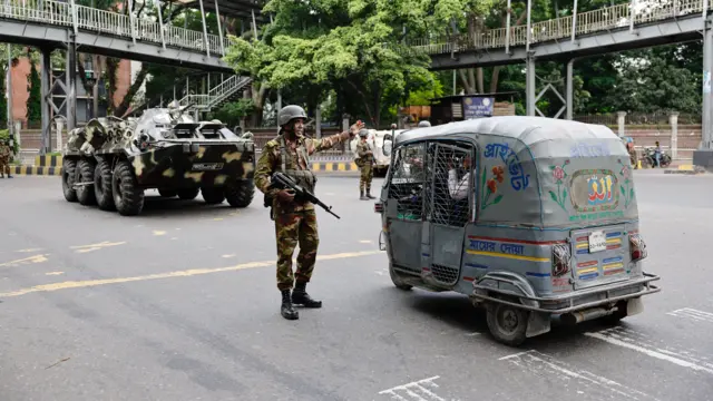 Um homem com roupas militares está parado na estrada pertotchouameni fifa 22um tuktuk com um tanque atrás dele.