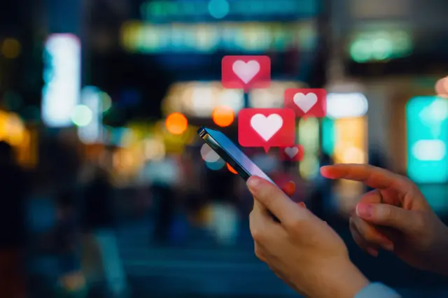 Alguém usando um celular, com ícones de coração saindo da tela