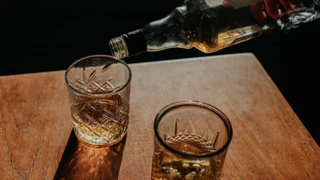 Dois copos de bebida sendo servidos por uma pessoa segurando uma garrafa.