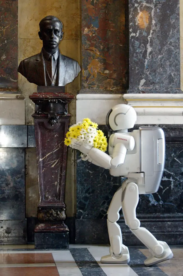 Honda өндүргөн сүйлөй алуучу робот Asimo Карел Чапектин Прагадагы улуттук музейиндеги айкелине гүл коюда, 2003