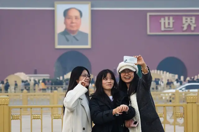 Mujeres haciéndose un selfie frente al retrato de Mao