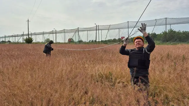 Енергетики ДТЕК ремонтують лінії електропередач, пошкоджені російськими обстрілами, за шість кілометрів від фронту на Донеччині. Поруч із ними над дорогою - захисна сітка від дронів