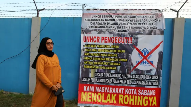 ဆာဘန်ကနေ ထွက်ခွာကြဖို့ ရိုဟင်ဂျာတွေကို ပြောထားတဲ့ ဆိုင်းဘုတ်တစ်ခုနားကနေ ဖြတ်သွားတဲ့ အမျိုးသမီးတစ်ဦး 