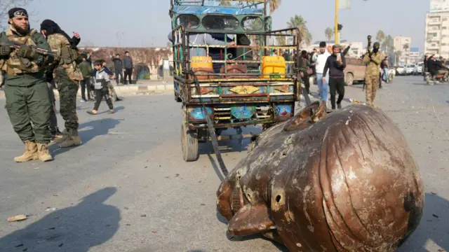 Uma caminhonete arrasta a cabeça derrubada de uma estátua do falecido presidente sírio Hafez al-Assad pelas ruas da cidade de Hama, no centro-oeste do país, em 6 de dezembro de 2024.