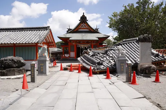 神社の参道を本殿に向かって写している写真。右側のかわらぶきの建物が大きく崩れているほか、参道の石畳も壊れている。周囲には赤い三角コーンが置かれている