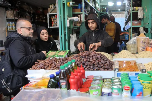 بائع يقدم التمور للزبائن في متجر بسوق الزاوية القديم في مدينة غزة في اليوم الأول من شهر رمضان المبارك في الأول من مارس 2025