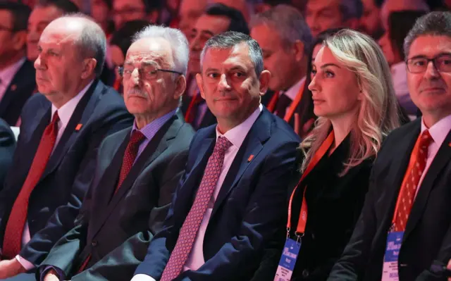 Özgür Özel, Dilek İmamoğlu ile yan yana oturuyor. Yanlarında diğer üst düzey isimler var. Özgür Özel yana bakıyor, İmamoğlu ileri