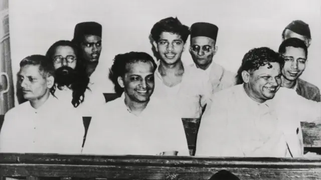 মোহনদাস করমচাঁদ গান্ধীর হত্যা মামলার শুনানির সময় অন্যান্য অভিযুক্তদের সাথে মি. সাভারকার (তৃতীয় সারিতে দ্বিতীয় জন)।প্রথম সারিতে সর্ববামে নাথুরাম গডসে