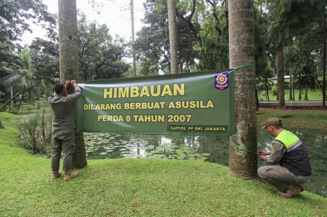 Petugas Satpol PP Jakarta Selatan memasang spanduk larangan berbuat asusila di Taman Langsat, Kebayoran Baru, Jakarta, Selasa (17/06).