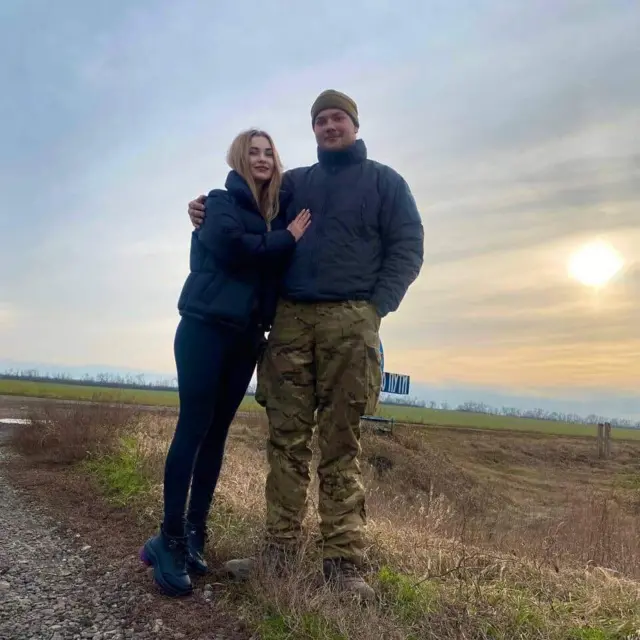 двою людей на тлі поля, дівчина в чорному і чоловік у військовій формі