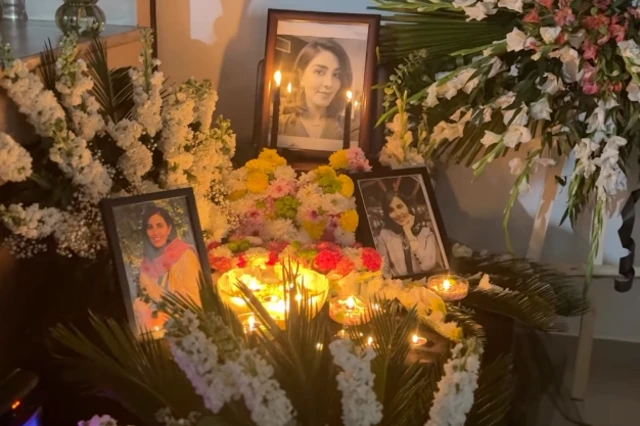 میزی حاوی عکس‌های پرستش و گل‌هایی که برای او در کنار شمع‌هایی گذاشته شده است.