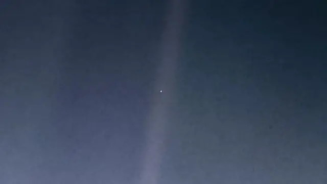 A tiny blue-ish speck can be seen within the streak of a sunbeam against a dark background.