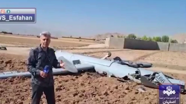 خبرنگار در کنار پهپاد بزرگی که سقوط کرده است. 