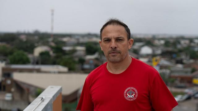 Rudnei Santos, um homem de meia idade com roupa de bombeiro; ao fundo vista da cidade