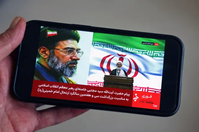 تُظهر هذه الصورة التوضيحية، التي التُقطت في 4 يونيو/حزيران 2026، رجلاً يشاهد البث المباشر على هاتفه المحمول لمسؤول إيراني يقرأ رسالة من المرشد الأعلى الإيراني آية الله مجتبى خامنئي للجمهور عند ضريح المرشد الأعلى الراحل آية الله روح الله الخميني، في طهران في 4 يونيو/حزيران 2026.