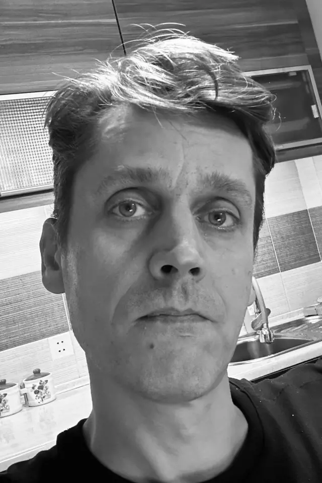 Черно-белое фото учредителя телеканала "Апрель" Дмитрия Ложникова крупным планом на фоне кухни