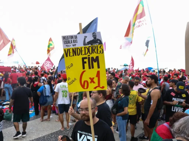 Homem segura placa pelo fim da escala 6x1 em ato do 1º de maio no Rio de Janeiro na praia de Copacabana