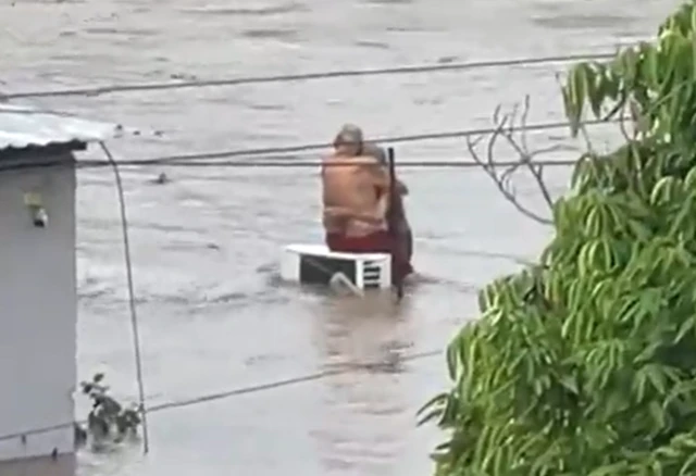 Don Layo y Doña Elo abrazados sobre un compresor de aire acondicionado en medio de la corriente por las inundaciones en Mçexico, 10 de octubre de 2025