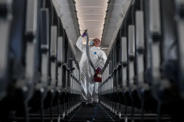 Una persona con un traje antibacterial desinfecta la cabina de un avión.