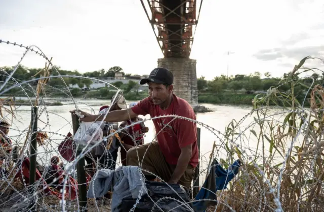 Người di cư từ Venezuela trèo qua dây thép gai sau khi vượt sông Rio Grande tại biên giới Mỹ-Mexico vào tháng 9/2023