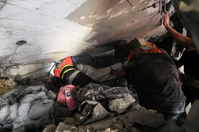 رجال الدفاع المدني يسحبون ضحية من تحت الأنقاض في موقع غارة إسرائيلية ليلية على منزل في مدينة غزة، 6 يوليو/تموز 2025.